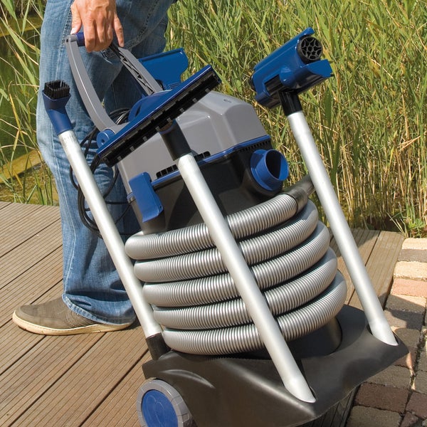 Schlammsauger mit aufgewickeltem Schlauch und Zubehör, transportiert von einer Person auf einem Holzdeck am Teich.