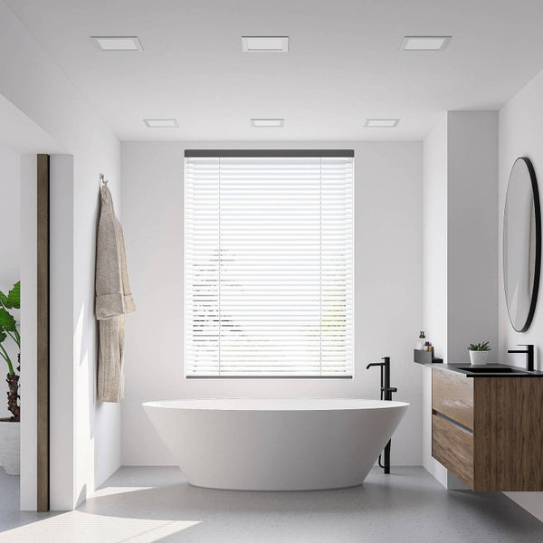 Modernes helles Badezimmer mit freistehender weißer Badewanne, Waschtisch aus Holz und weißer Jalousie am Fenster.