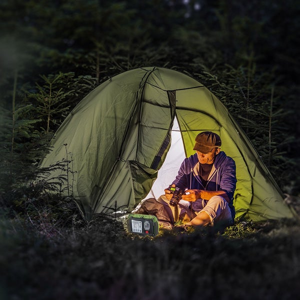 Szene mit einem Mann vor einem Zelt im Wald, daneben eine tragbare Stromversorgung.