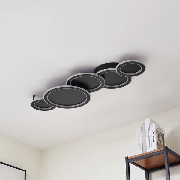 Moderne dunkelgraue Deckenleuchte mit fünf überlappenden Kreiselementen und LED-Lichtringen in einem hellen Raum über einem Bücherregal.
