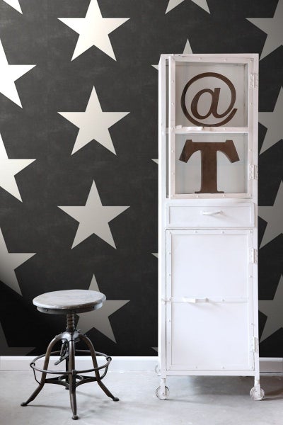 Szene mit einem Hocker, einem weißen Schrank mit Metallzeichen und einer Tapete mit Sternenmuster