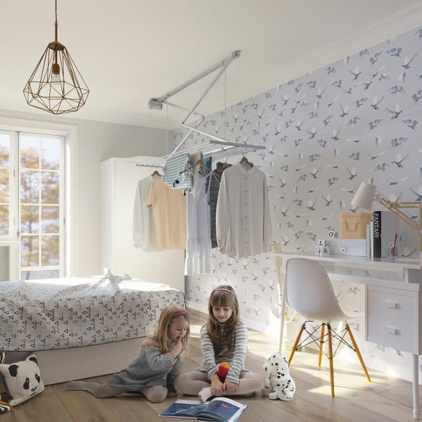 Ein helles Kinderzimmer mit einem Deckentrockner, Wäsche, einem Bett, einem Schreibtisch und zwei spielenden Mädchen