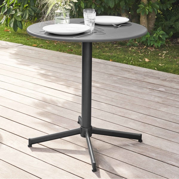 Runder Bistro-Gartentisch aus Metall auf einer Holzterrasse, gedeckt für zwei Personen vor Gartenkulisse.