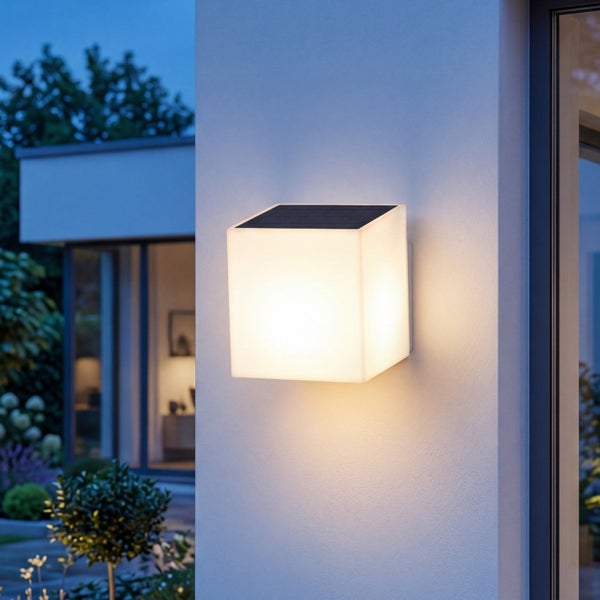 Moderne quadratische Solar Wandleuchte für den Außenbereich, montiert an einer Hausfassade, mit warmweißem Lichtschein bei Dämmerung.
