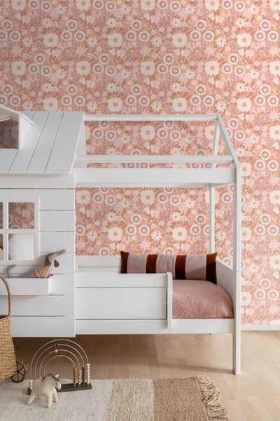 Kinderzimmer mit floral gemusterter Tapete, weißem Hausbett aus Holz und Spielzeug auf hellem Holzboden.