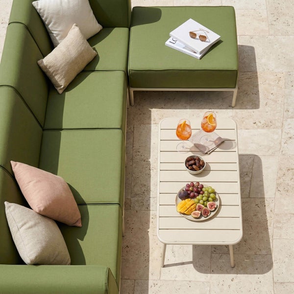 Grüne Gartenlounge mit Ecksofa, Hocker und Loungetisch auf einer hellen Steinterrasse.