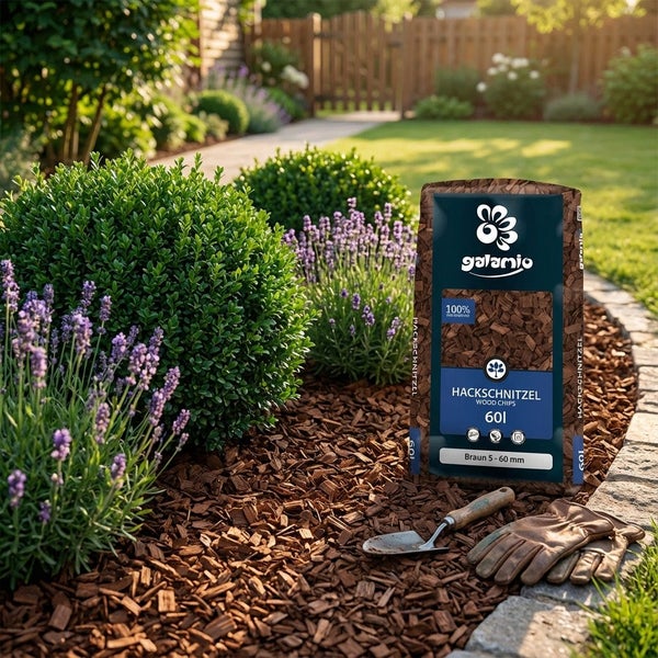 Galamio Hackschnitzel im 60 Liter Sack als Gartenmulch, platziert neben einer Gartenschaufel und Gartenhandschuhen im bepflanzten Beet.