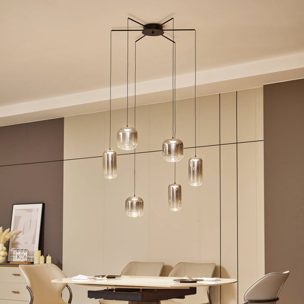 Moderne Pendelleuchte mit sechs rauchglasfarbenen Glasschirmen an einer schwarzen Deckenhalterung über einem Esstisch.