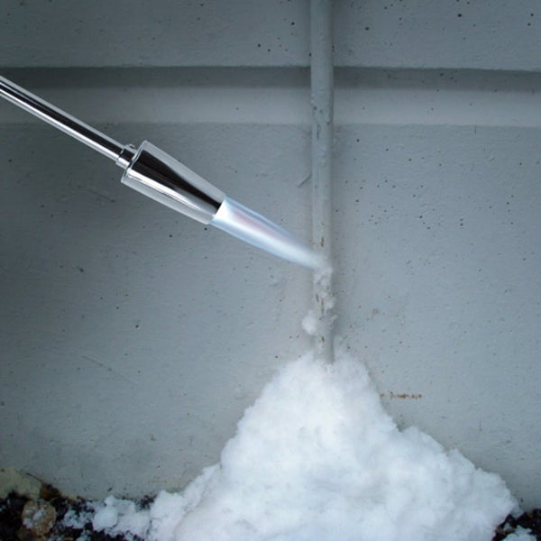 Außenaufnahme eines Mannes, der mit einem Unkrautbrenner einen gepflasterten Weg reinigt, der zu einem Haus führt.