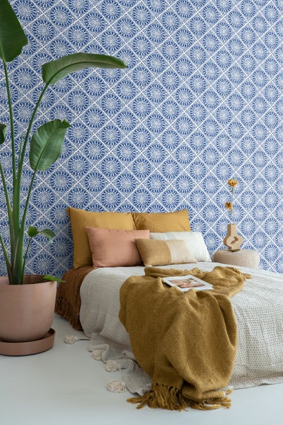 Schlafzimmer mit blau gemusterter Tapete, Bett, Kissen und Zimmerpflanze im Topf