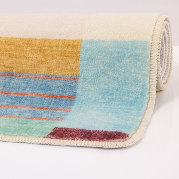 Teilweise aufgerollter Teppich mit geometrischem Muster, Streifen und Farbblöcken, weicher Flor und gekettelter Rand.