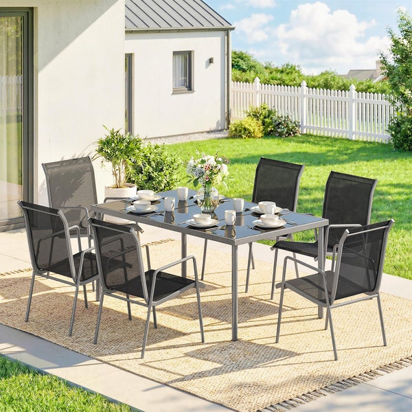 Gartensitzgruppe mit rechteckigem Glastisch und sechs Stühlen mit Textilbespannung auf einem Außenteppich in einem hellen Garten.