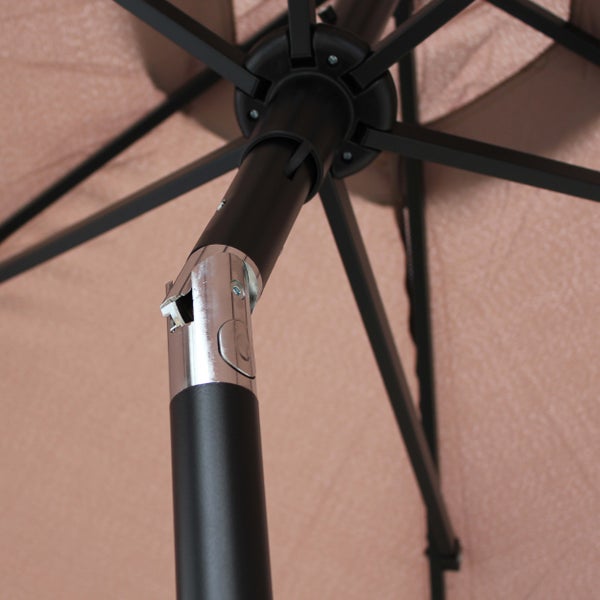 Beiger Sonnenschirm über einem Gartentisch mit schwarzen Stühlen auf einer Terrasse vor einer grünen Hecke und Rasenfläche.