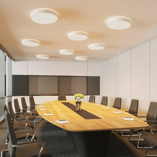 Moderner Besprechungsraum mit mehreren runden LED-Deckenleuchten in verschiedenen Größen, einem ovalen Holztisch und dunklen Bürostühlen.