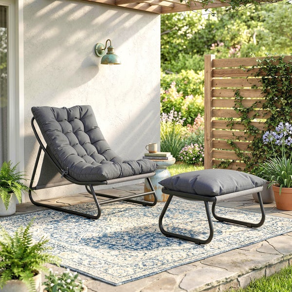 Outdoor-Loungesessel mit passendem Hocker, dunkelgraue Polsterauflagen auf Metallgestell, auf einer Terrasse mit Pflanzen und Outdoor-Teppich.