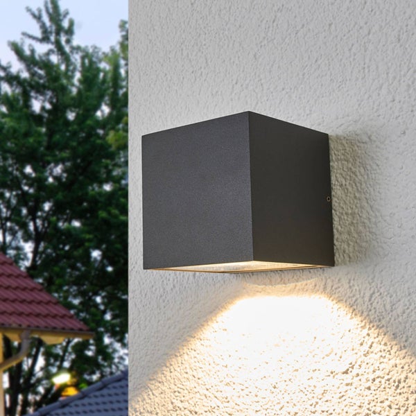 Moderne würfelförmige Außenwandleuchte an einer weißen Fassade mit Lichtschein nach unten.