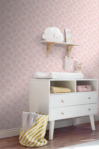 Vliestapete mit floralem Muster aus Gänseblümchen in einem hell eingerichteten Kinderzimmer mit weißer Wickelkommode und Wandregal.