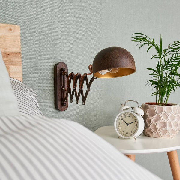 Szene mit Bett, Nachttisch, Wandleuchte, Wecker und Zimmerpflanze.