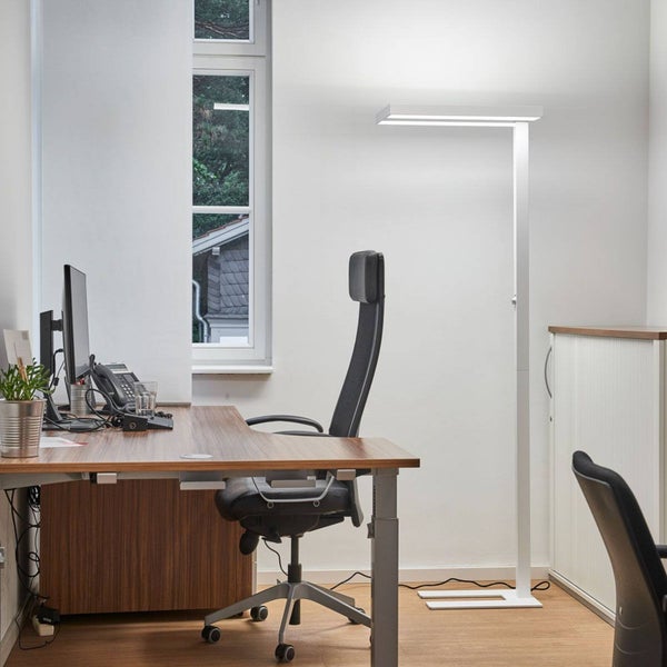 Moderne weiße LED-Bürostehleuchte in einem hellen Büro mit Holzschreibtisch, ergonomischem schwarzem Stuhl und einem Fenster.