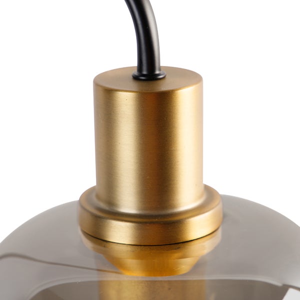 Nahaufnahme einer Pendelleuchte mit goldfarbener Fassung, schwarzem Kabel und grauem Glasschirm.