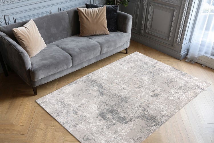 Rechteckiger Teppich mit abstraktem Muster vor einem grauen Sofa im Wohnzimmer mit Fischgrätparkett
