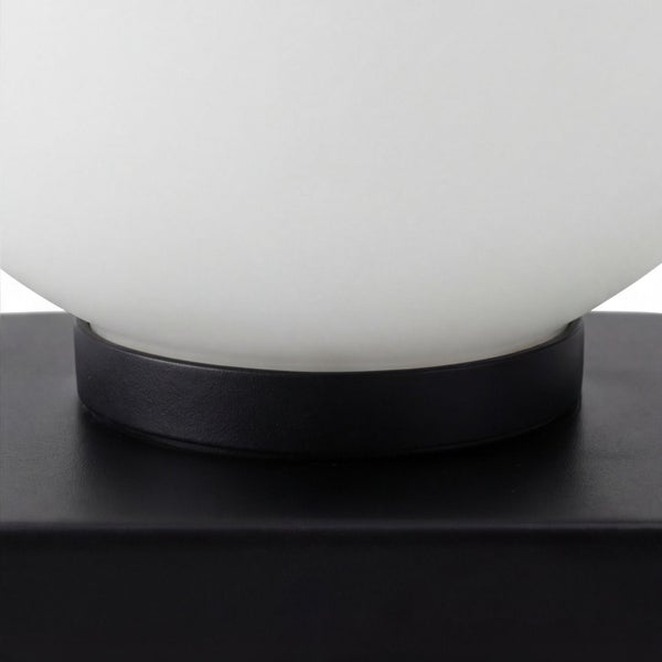 Detailansicht einer runden weißen Glasleuchte auf einem schwarzen Metallsockel.