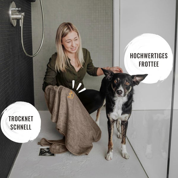 Frau trocknet Hund mit einem schnelltrocknenden Frotteehandtuch im Badezimmer ab.