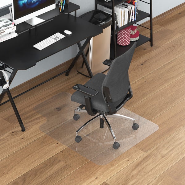 Transparente Bodenschutzmatte für Hartböden unter einem schwarzen Schreibtisch mit ergonomischem Bürostuhl in einem hellen Arbeitszimmer.