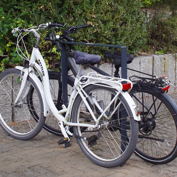 Zwei Fahrräder, darunter ein weißes Kettler Fahrrad, stehen an einem Fahrradständer.