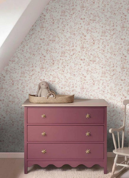 Vliestapete mit floralem Muster und Hasenmotiven in einem Kinderzimmer hinter einer Kommode mit Sternknöpfen und einem Stofftier.