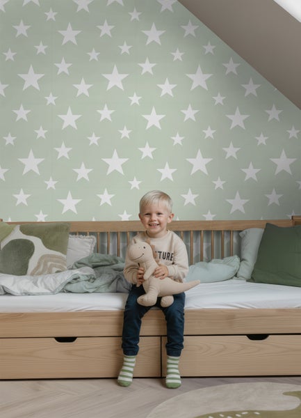 Vliestapete mit weißen Sternen auf grünem Hintergrund in einem hellen Kinderzimmer mit Holzbett.
