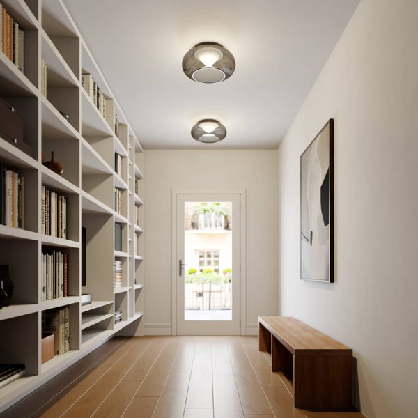 Hell gestalteter Flur mit zwei runden Deckenleuchten, einem großen weißen Bücherregal und Holzboden.