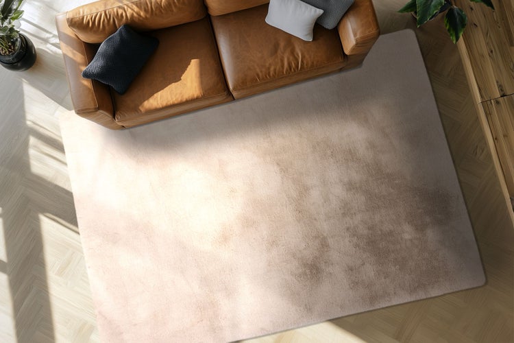 Draufsicht auf ein Wohnzimmer mit einem modernen Teppich vor einem Ledersofa auf einem Parkettboden.