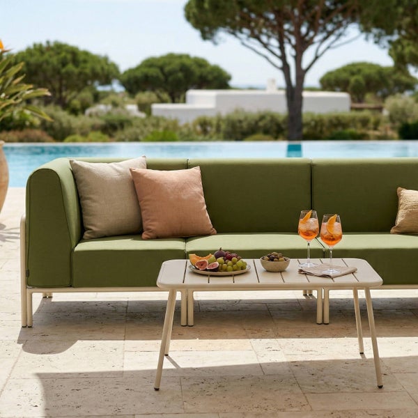Moderner Außenbereich mit grünem Lounge-Sofa, Beistelltisch und Pool im Hintergrund auf einer hellen Steinterrasse.