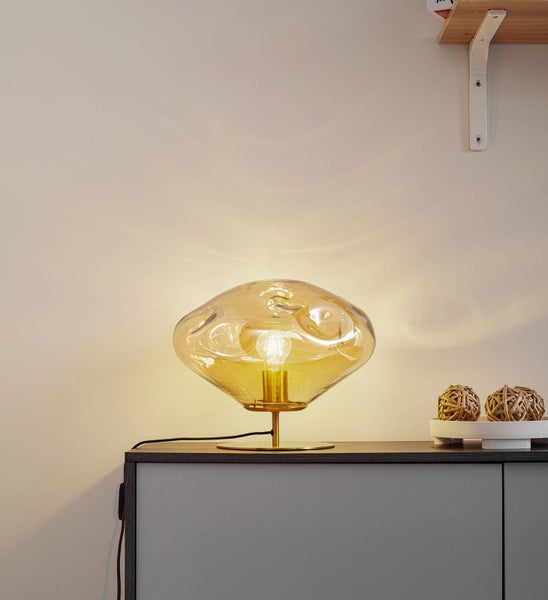Moderne Tischleuchte mit organisch geformtem, getöntem Glasschirm und Metallfuß, platziert auf einem Sideboard im Wohnbereich.