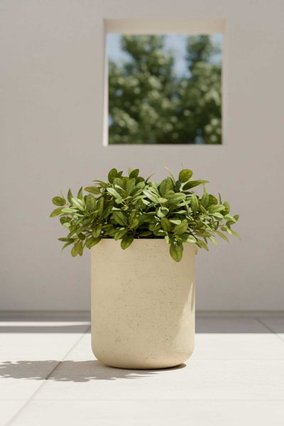 Zylindrischer, beiger Pflanzkübel mit strukturierter Oberfläche und grüner Pflanze auf einer hellen, minimalistischen Terrasse.