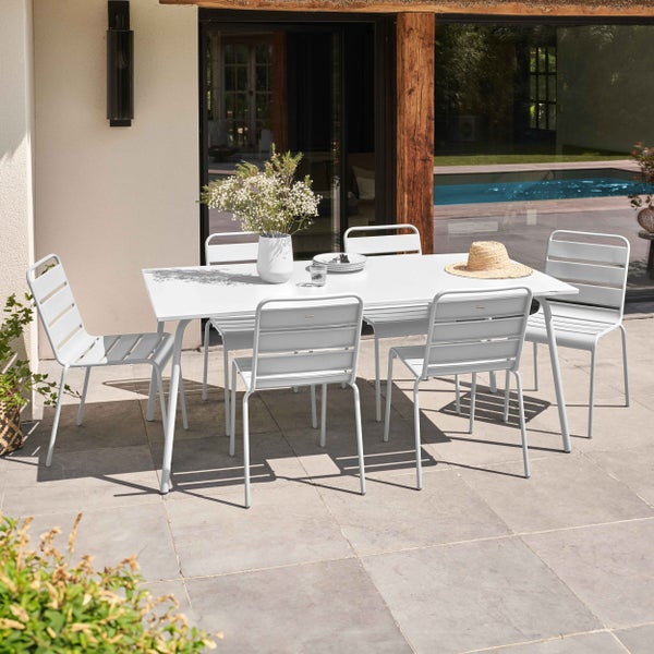 Modernes Gartenmöbel-Set bestehend aus einem weißen rechteckigen Tisch und sechs weißen Gartenstühlen aus Metall auf einer Terrasse am Pool.