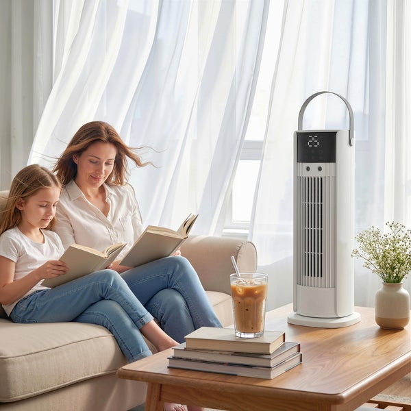 Weißer Turmventilator mit Digitalanzeige auf einem Holztisch in einem hellen Wohnzimmer, während eine Frau und ein Kind auf dem Sofa lesen.