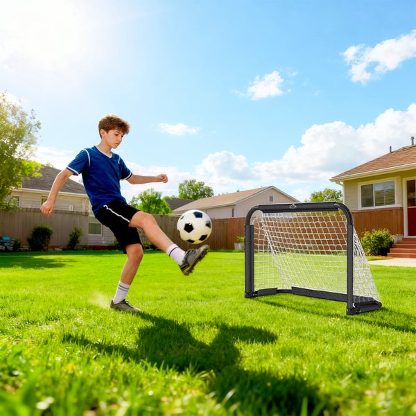 Ein Junge spielt mit einem kleinen Fußballtor im Garten auf dem Rasen bei sonnigem Wetter.