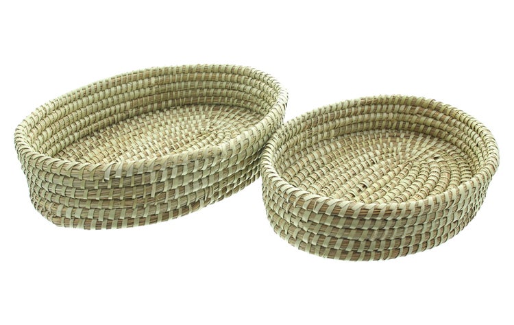 Zwei flache, geflochtene Aufbewahrungskörbe aus Naturmaterial in ovaler und runder Form.