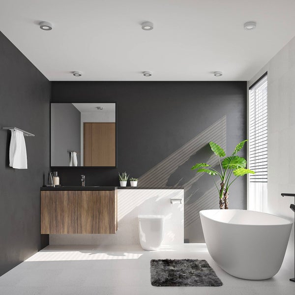 Modernes, helles Badezimmer mit freistehender weißer Badewanne, wandhängendem Waschtisch in Holzoptik und dunklen Wänden.