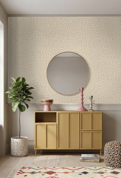 Helles Zimmer mit Vliestapete im Leopardenmuster, einem runden Spiegel, einem gelben Sideboard und einer Zimmerpflanze.