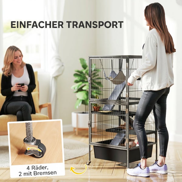 Eine Frau schiebt einen hohen Kleintierkäfig auf Rollen in einem hellen Wohnzimmer. Der Käfig hat vier Räder, zwei davon mit Bremsen.