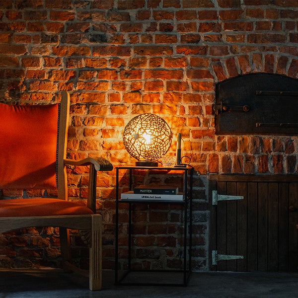 Szene mit Backsteinmauer, Stuhl, Tisch und dekorativer Tischleuchte.