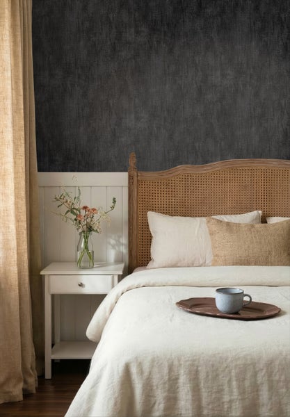 Schlafzimmer mit dunkler Strukturtapete über weißem Paneel. Bett mit Geflecht-Kopfteil, weißer Nachttisch und helle Bettwäsche.