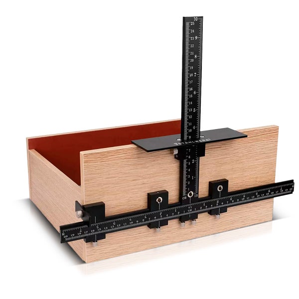 Schwarze Bohrschablone aus Metall für Möbelgriffe, montiert an einer Holzschublade, mit Zentimeter- und Zoll-Skala.