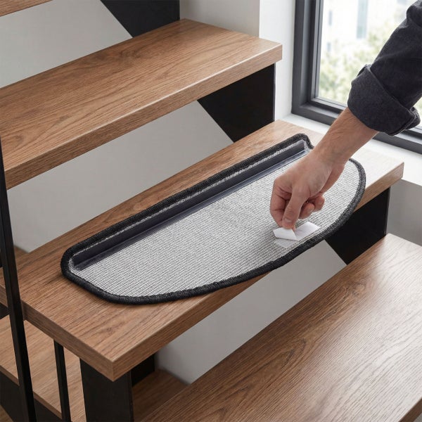 Eine Person bringt eine Treppenstufenmatte mit Klebestreifen auf einer Holztreppe an.