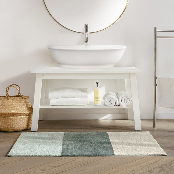 Badezimmer mit Waschbecken, Spiegel, Handtüchern, Korb und Badteppich