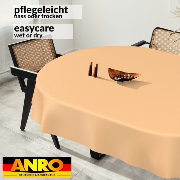 Rundes, pflegeleichtes Tischtuch auf einem modernen Esstisch mit Rattanstühlen. Nass oder trocken abwischbar. ANRO Deutsche Manufaktur Logo.