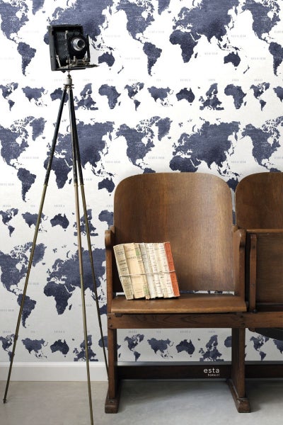 Raumansicht mit Weltkarten-Tapete, alter Kamera auf Stativ und hölzernen Kinostühlen mit Büchern